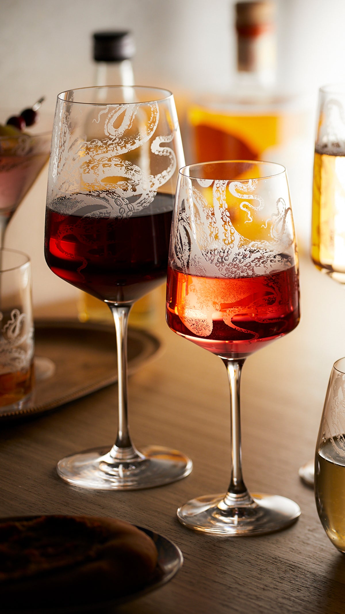 Two stemmed wine glasses, one with red wine and one with rose, in crystal etched with the Lucy the Octopus pattern from Caskata