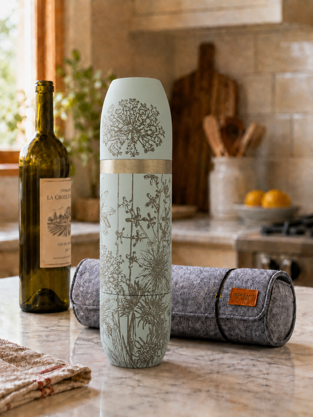 Caskata x High Camp wine flask in Summer Wildflowers pattern in light blue (Granite) on a kitchen counter with it's wool case