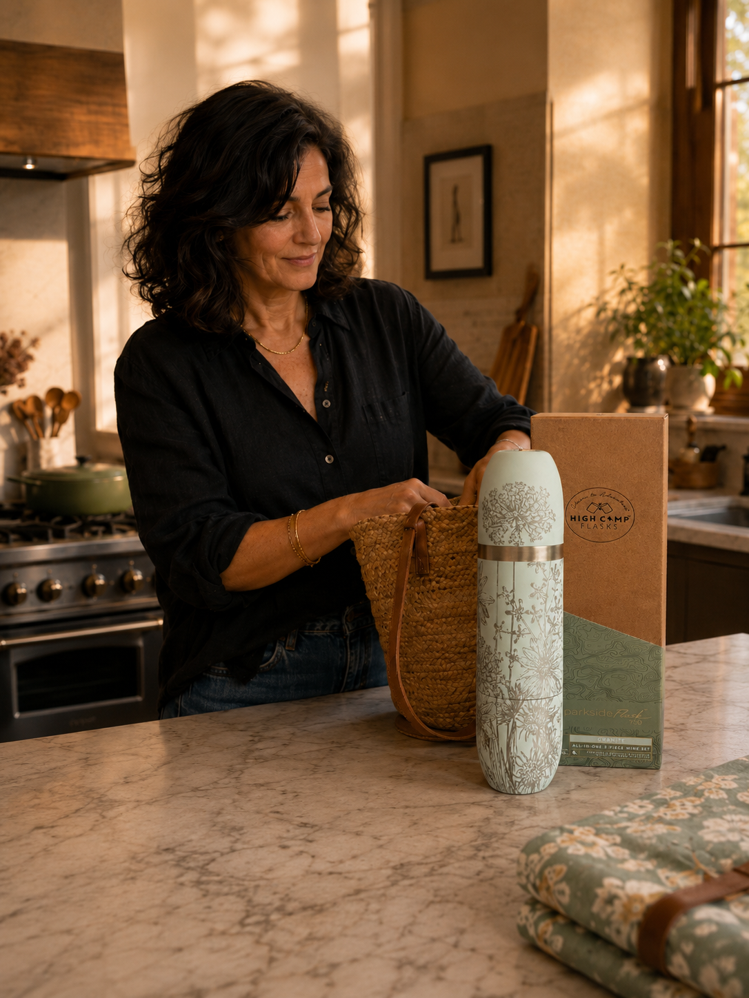 Jackie, a Caskata customer, at home in her kitchen with the Caskata x High Camp Summer flask in Granite on the counter.