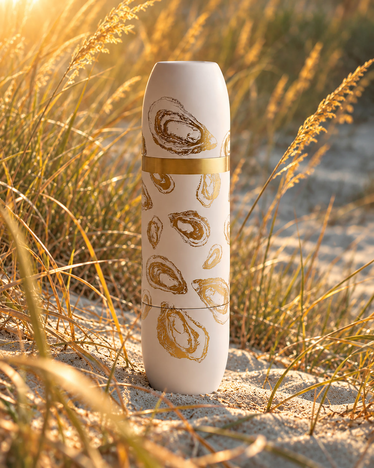 Caskata x High Camp Oyster Wine Flask in Cream with gold engraving on a dune in golden hour amidst the dune grass.