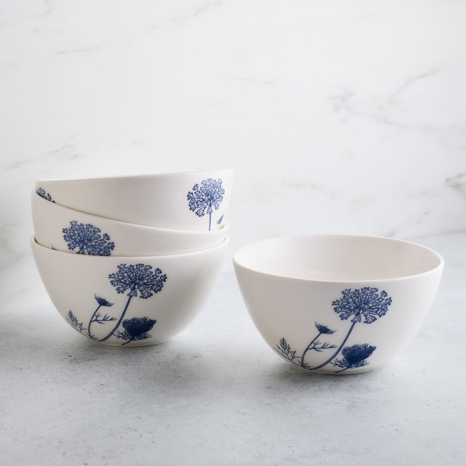 The Caskata Summer Blues Table for 4 is a porcelain dinnerware set featuring six blue and white botanical plates and six matching bowls with elegant floral designs, all displayed on a white background.