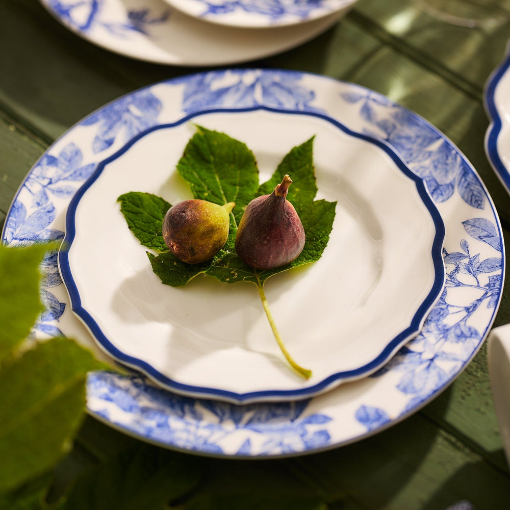 Two figs rest on a fig leaf, artfully centered on a decorative Stella Scalloped Blue Salad Plate by Caskata.