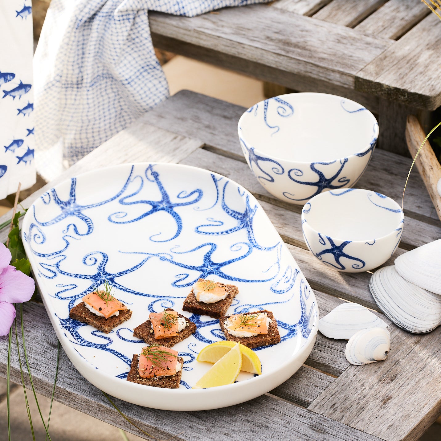 The Caskata Starfish Crudité Set includes an oval porcelain platter and small bowl with a blue starfish pattern on white—perfect as a serving or appetizer dish.