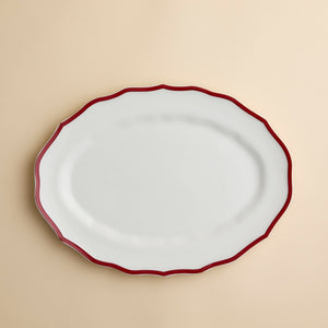 Caskata Stella Crimson Scalloped Platter in white porcelain with an oval shape and a thin red rim.