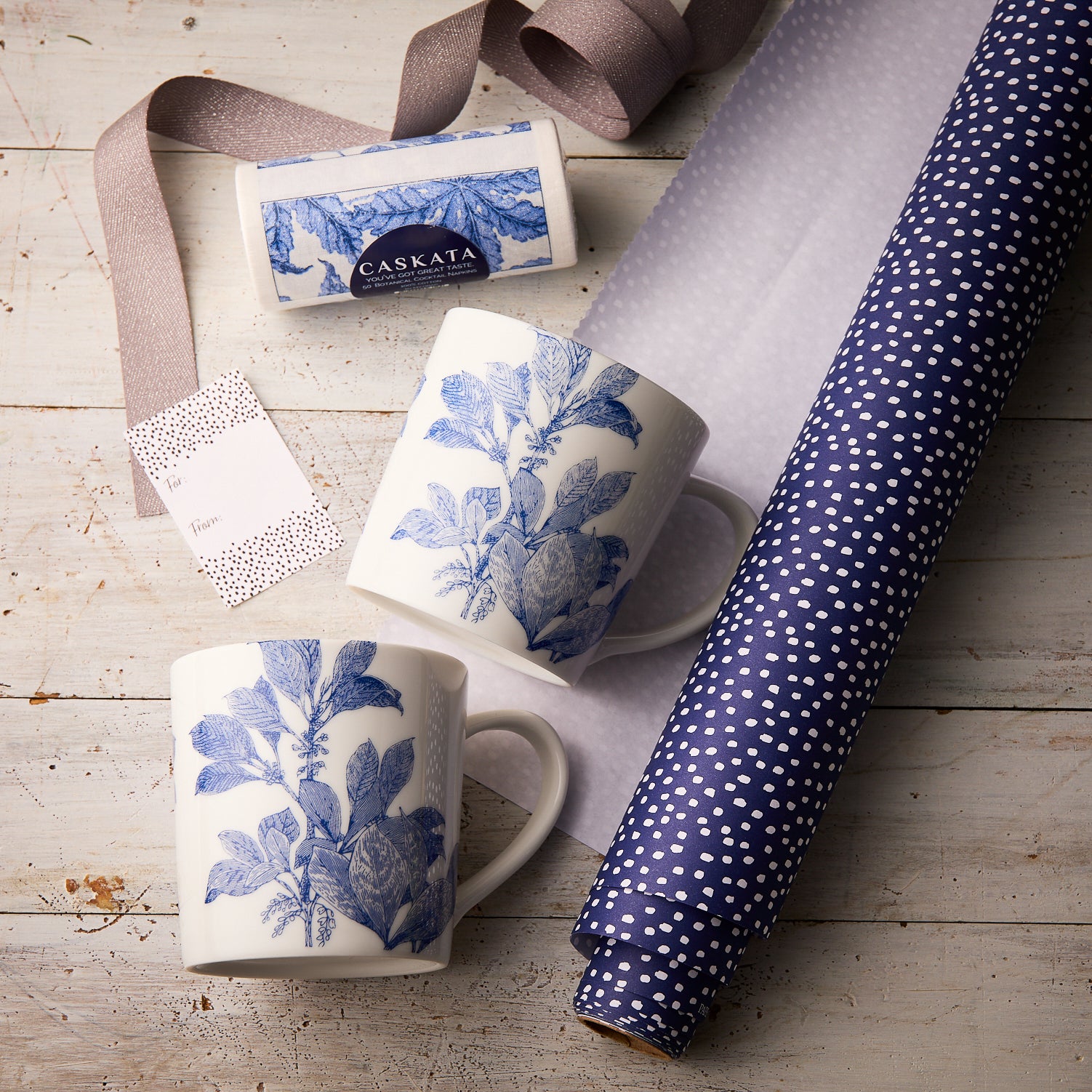 The Caskata Arbor Coffee Talk Bundle features two blue botanical porcelain mugs, a purple polka dot gift wrap roll, lavender ribbon, and a Caskata soap bar—perfect for coffee lovers.