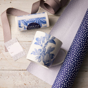 The "Arbor Day" Bundle by Caskata features a porcelain mug with blue botanical design, patterned wrapping paper, ribbon, gift tag, boxed soap, and a matching cocktail napkin artfully arranged for a charming gift set.