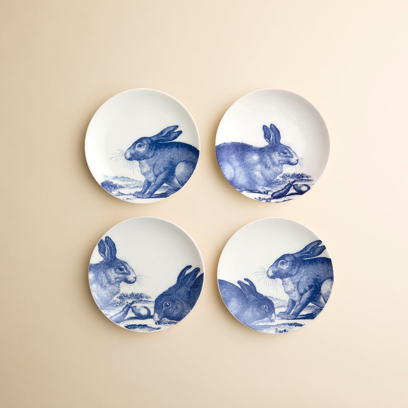 A set of 4 small appetizer plates from Caskata in their Bunnies blue pattern highlight four different rabbit engravings on high-fired porcelain dinnerware.
