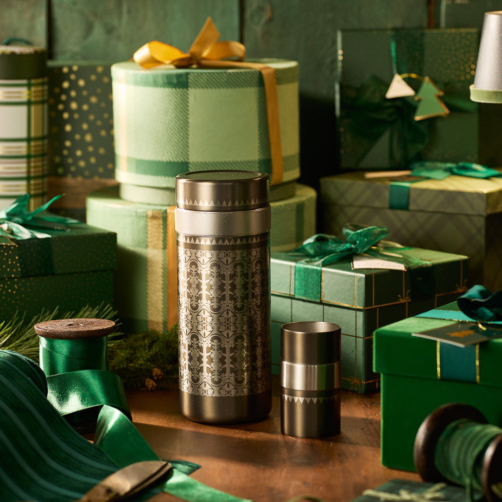 The Caskata x High Camp Casablanca Batch Cocktail Shaker by Caskata, shown with its lid off amid green and gold gift boxes, ribbons, and festive decor on wood, makes a stylish bar gadget or extra-large cocktail shaker for celebrations.