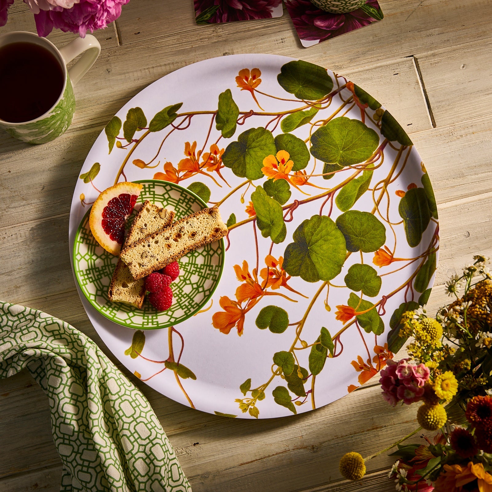 A white plate with an orange and green floral pattern sits beside a tall glass filled with greens, both on a white background—the perfect accents for your Caskata Gardener's Essentials Bundle.