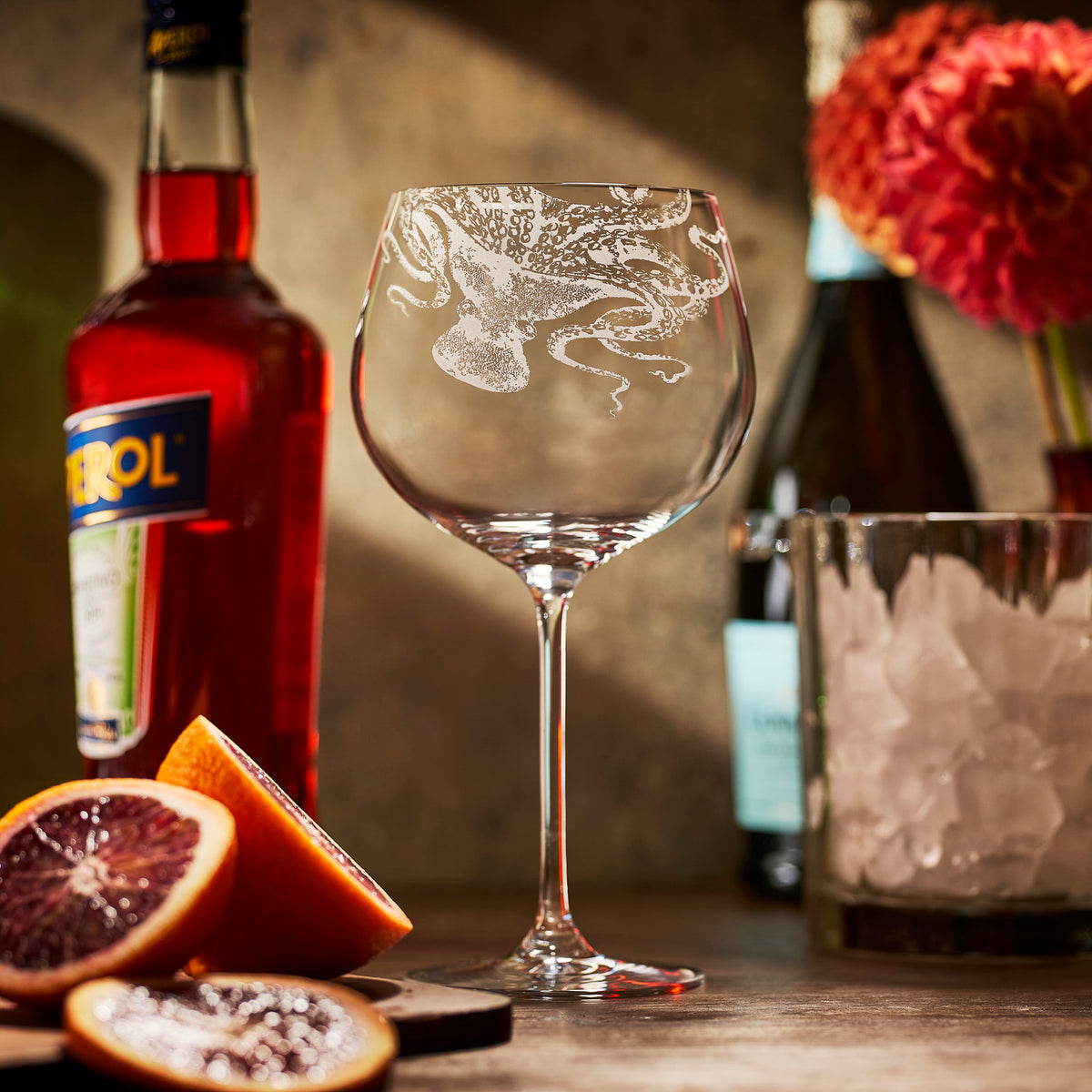 Caskata's Lucy the Octopus Crystal Etched Gin & Tonic glass ready to be filled on a tabletop with Aperol in the background