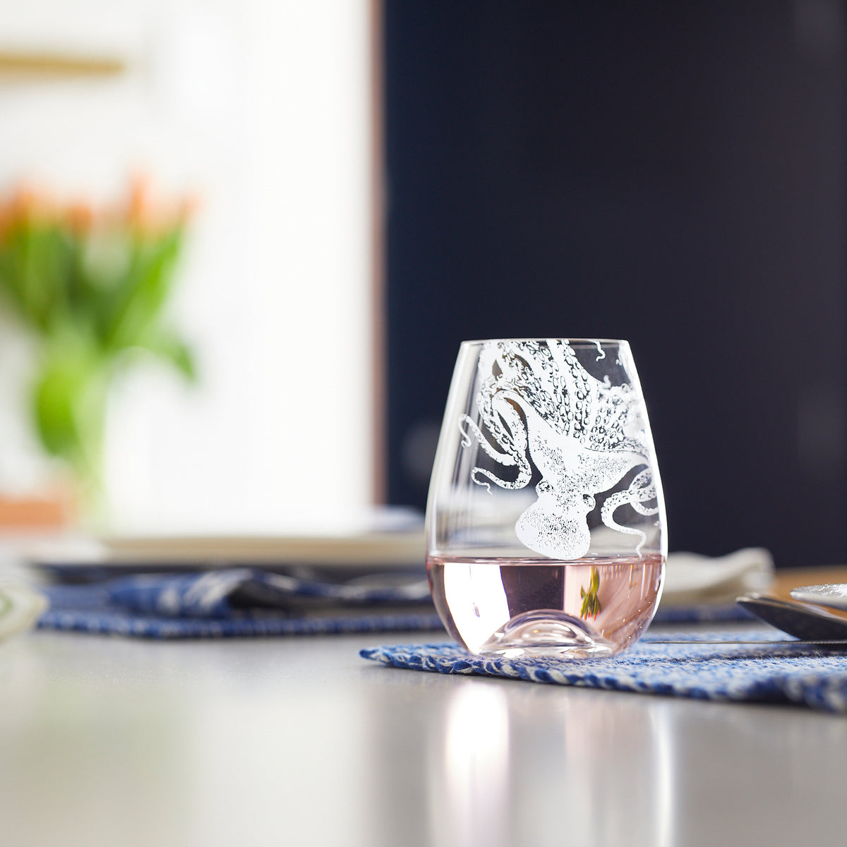 Caskata's Lucy the Octopus Stemless wine glass with a light colored wine on a kitchen counter in etched crystal from Europe.