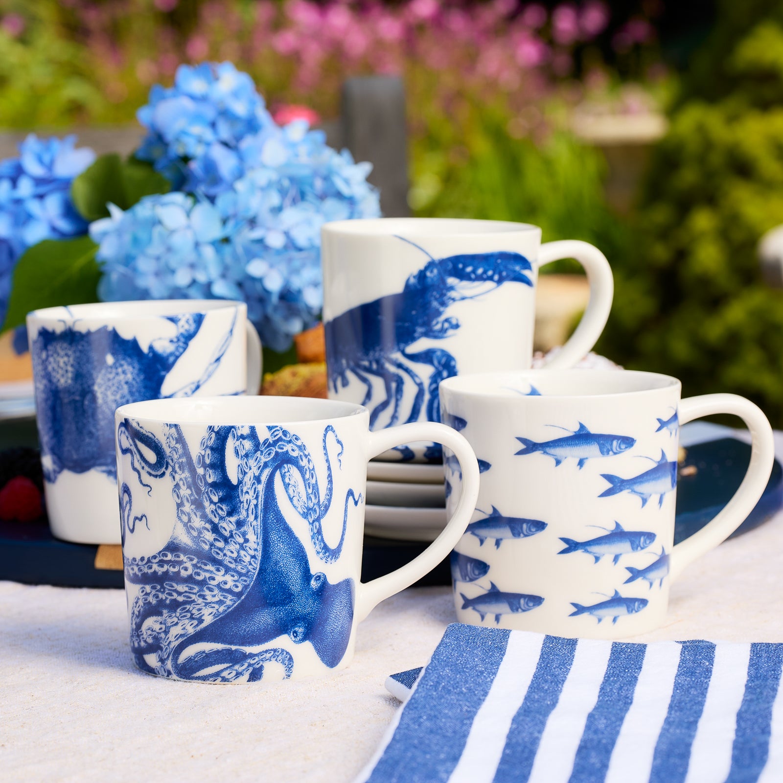 Coastal Mugs in a series of iconic prints including School of Fish, Lobster, Crab, and Lucy the Octopus in blue on creamy white porcelain from Caskata in a mixed set of 4.