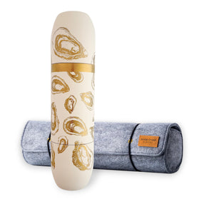 The Caskata x High Camp Crema Oysters Wine Flask and Case Bundle from Caskata is shown, featuring a cream-colored wine flask adorned with gold oyster designs, placed in front of a gray felt carrying case with a leather label.