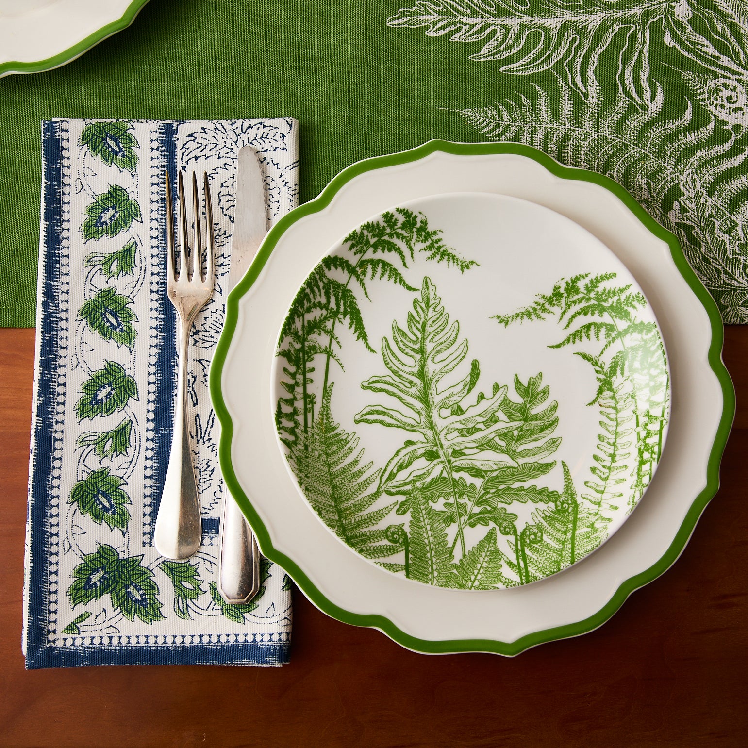 The Caskata Spring Verde Coupe Salad Plate is a round white porcelain plate adorned with a green fern leaf design, bringing elegant botanical style to any table.