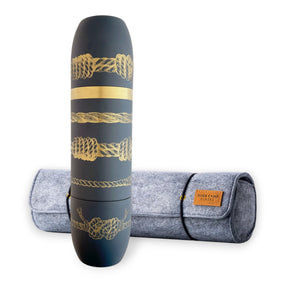 A Caskata x High Camp Dark Blue Sailor's Knots Wine Flask, adorned with elegant gold rope designs, stands upright in front of a rolled grey felt case labeled "High Camp Flasks." This insulated wine flask from caskata.mombines nautical flair with functionality, making it an ideal choice for adventurers and wine enthusiasts alike.