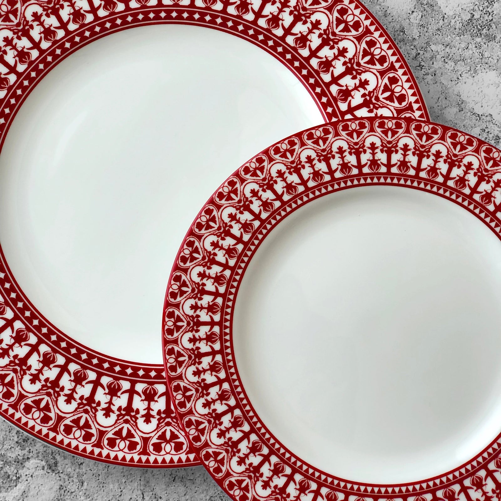 The Casablanca Crimson Table for 4 by Caskata is a 12-piece porcelain set with six large plates, six small plates, and six bowls, each featuring a red and white geometric pattern with ornate scrollwork on the rims.