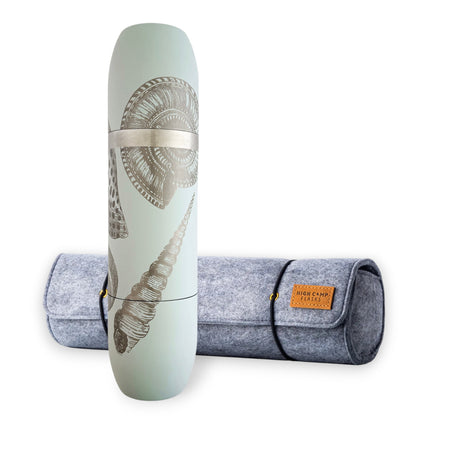 A Caskata x High Camp Light Blue Shells Wine Flask and Case Bundle stands upright next to a rolled-up gray felt carrying case with a brown leather label, the shell patterns on the flask perfectly matching your yoga mat for the ideal post-session refreshment.