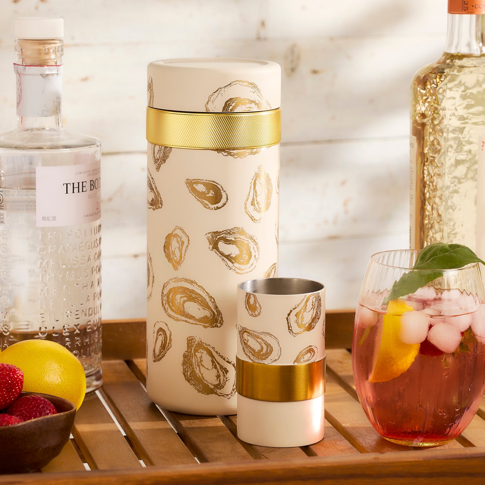 The Caskata x High Camp Oysters Batch Cocktail Shaker by Caskata—a white, vacuum-insulated shaker with gold oyster designs—sits beside its chic black-and-gold box, making a stylish bar accessory.