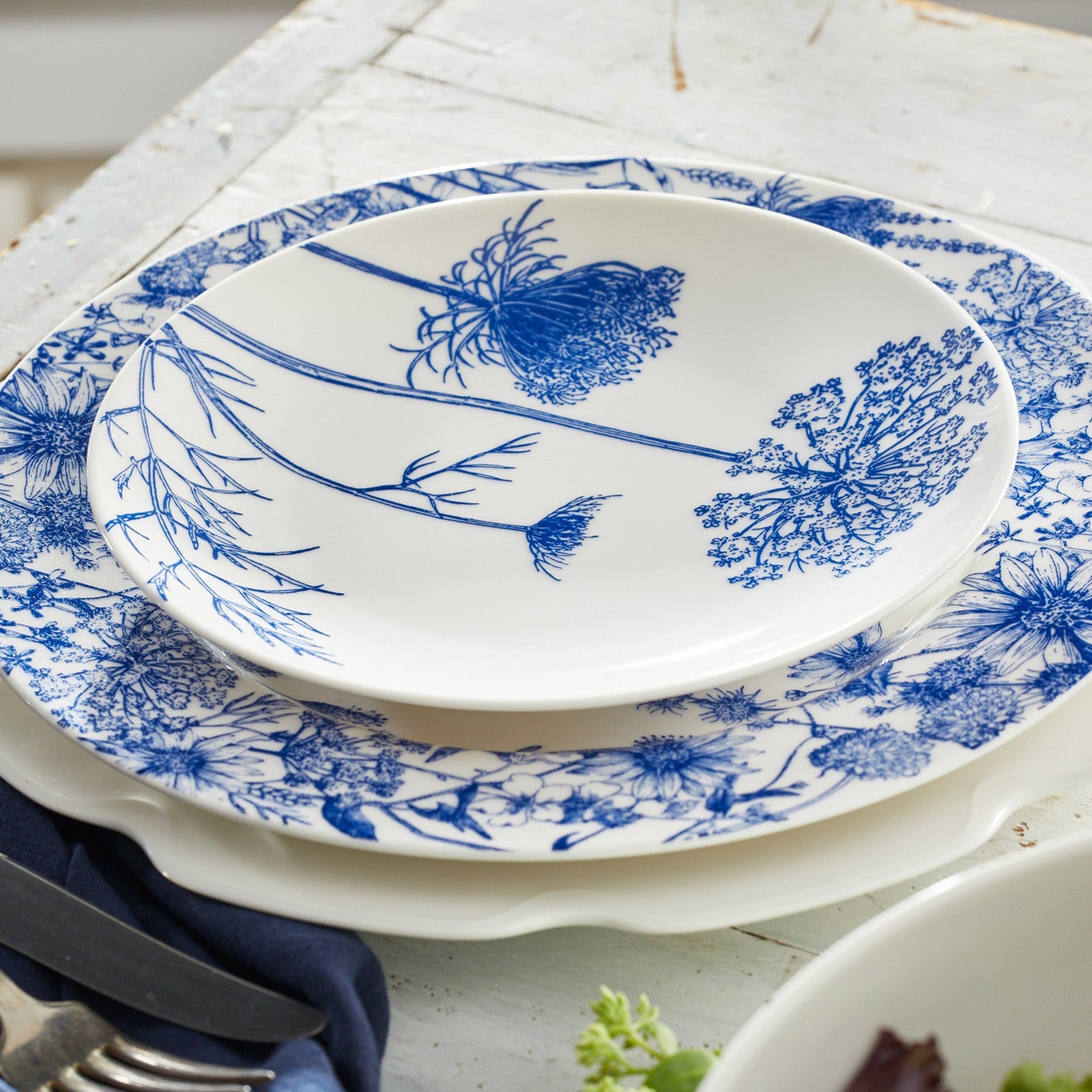 The Summer Blues Table for 8 by Caskata is a 24-piece porcelain dinnerware set with six oval platters, six round plates, and six bowls, all featuring elegant blue and white floral patterns.