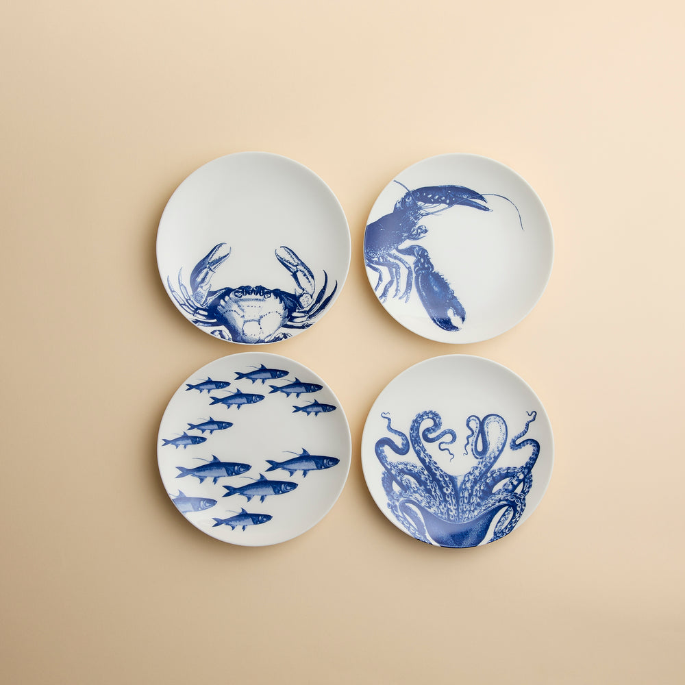 A set of four dishwasher-safe porcelain Coastal Icons Small Plates, Mixed Set of 4, each featuring a blue marine life illustration of a crab, lobster, school of fish, or octopus.