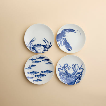 A set of four dishwasher-safe porcelain Coastal Icons Small Plates, Mixed Set of 4, each featuring a blue marine life illustration of a crab, lobster, school of fish, or octopus.