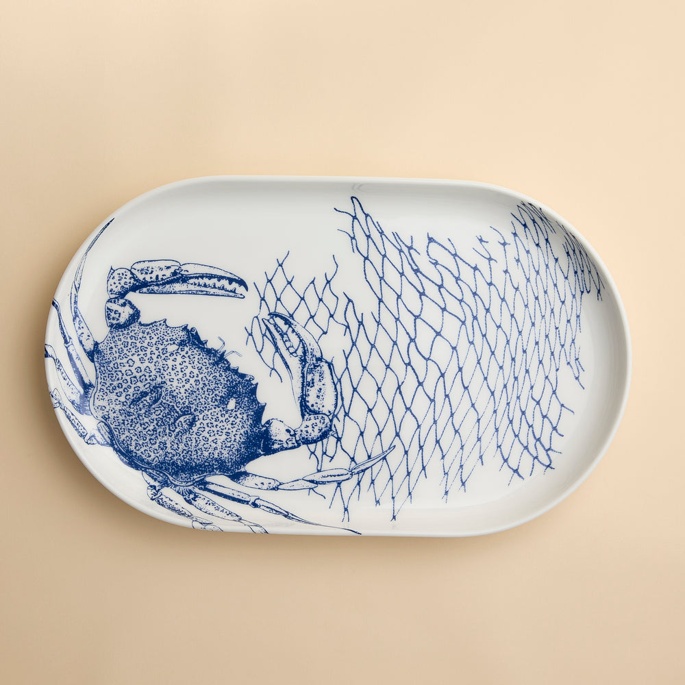 Crabs and nets sprawl across this contemporary coupe oval platter in blue and white high-fired porcelain from Caskata.
