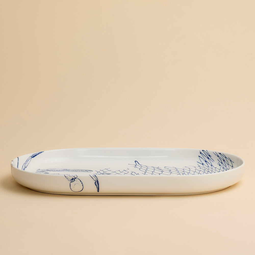 Caskata’s Crab Large Coupe Oval Platter, featuring elegant blue line art of a crab on porcelain, is photographed against a plain beige background. This refined serving piece brings coastal charm to any table setting.