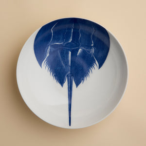 Caskata’s Horseshoe Crab Entrée Bowl—a white oval plate adorned with a blue horseshoe crab illustration viewed from above—adds exquisite coastal charm and seaside elegance to any table setting.