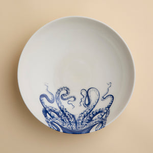 White ceramic plate featuring a blue octopus tentacle design on one side, set atop a beige surface—a striking piece that pairs beautifully with the Lucy Entrée Bowl by Caskata Artisanal Home or any other blue and white bowl in your collection.