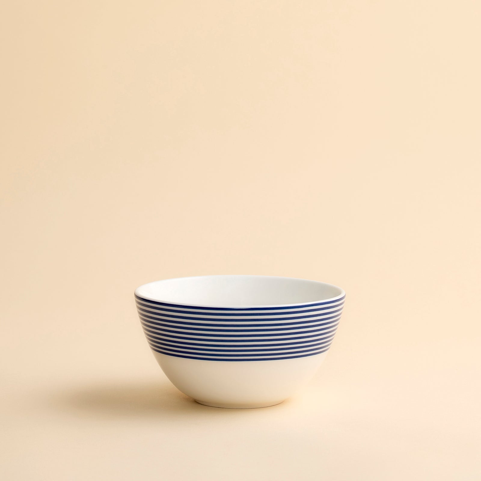 Caskata Newport Stripe cereal bowl in porcelain white featuring horizontal blue stripes around the upper half against a creamy beige background.