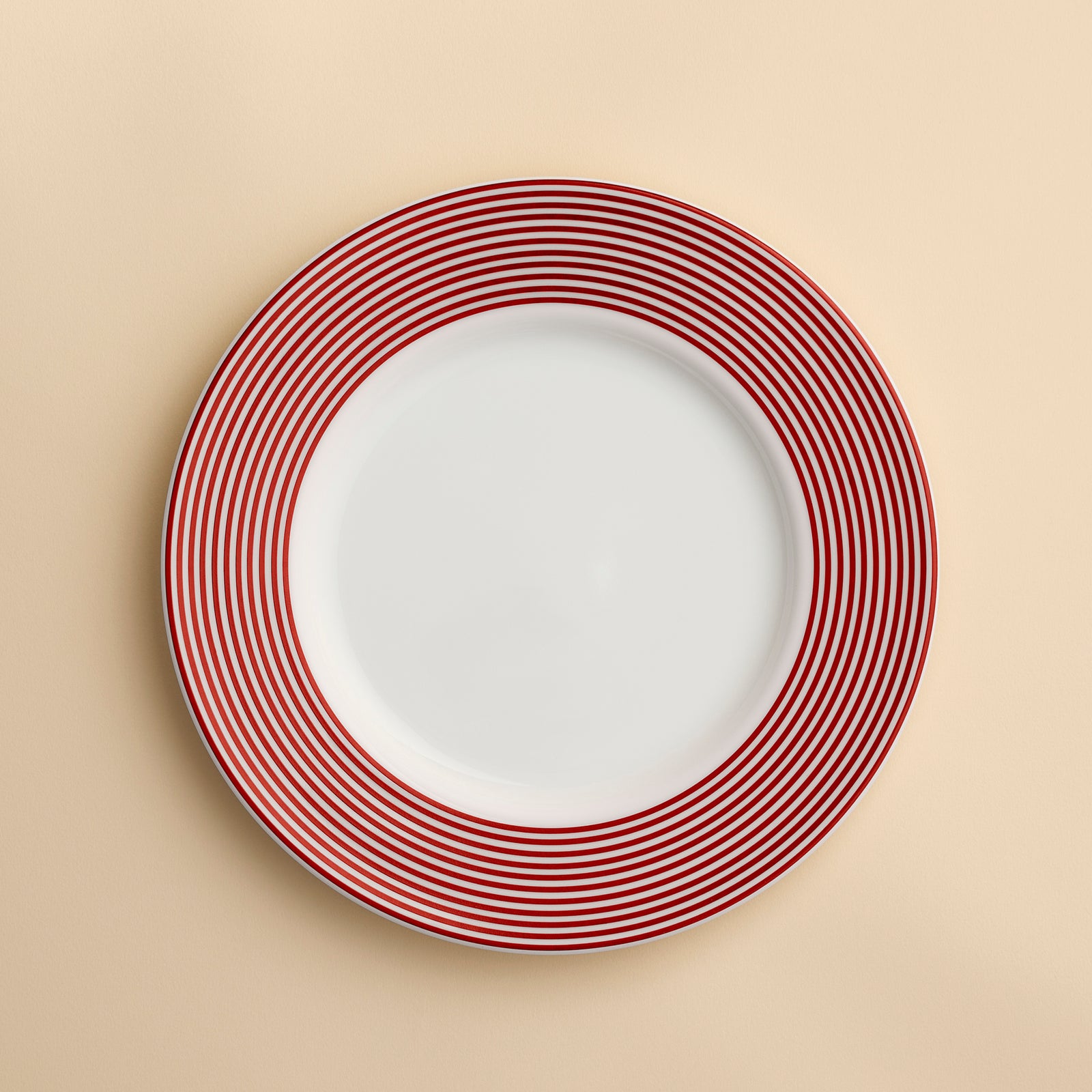 A Newport Crimson Stripe Salad with concentric rings of red stripes around the rim of this high-fired porcelain plate from Caskata, shown against a creamy beige background.