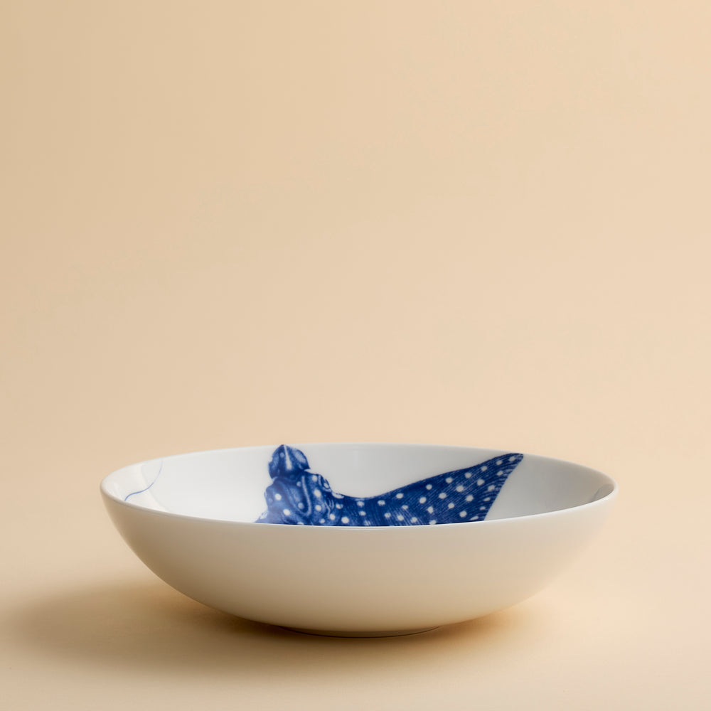 The Caskata Ray the Stingray Entrée Bowl features a white porcelain design with a blue stingray illustration on the inside, set against a plain beige background. This dinnerware piece is both dishwasher and microwave safe.