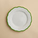 The Caskata Stella Scalloped Verde Salad Plate features high-fired porcelain with a scalloped green rim, shown from above on a beige background. This plate adds elegant, vintage-inspired charm to any table setting.