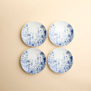 Set of 4 Summer Blues Small Plates by Caskata, crafted from high-fired porcelain with blue floral designs, are arranged against a creamy beige background