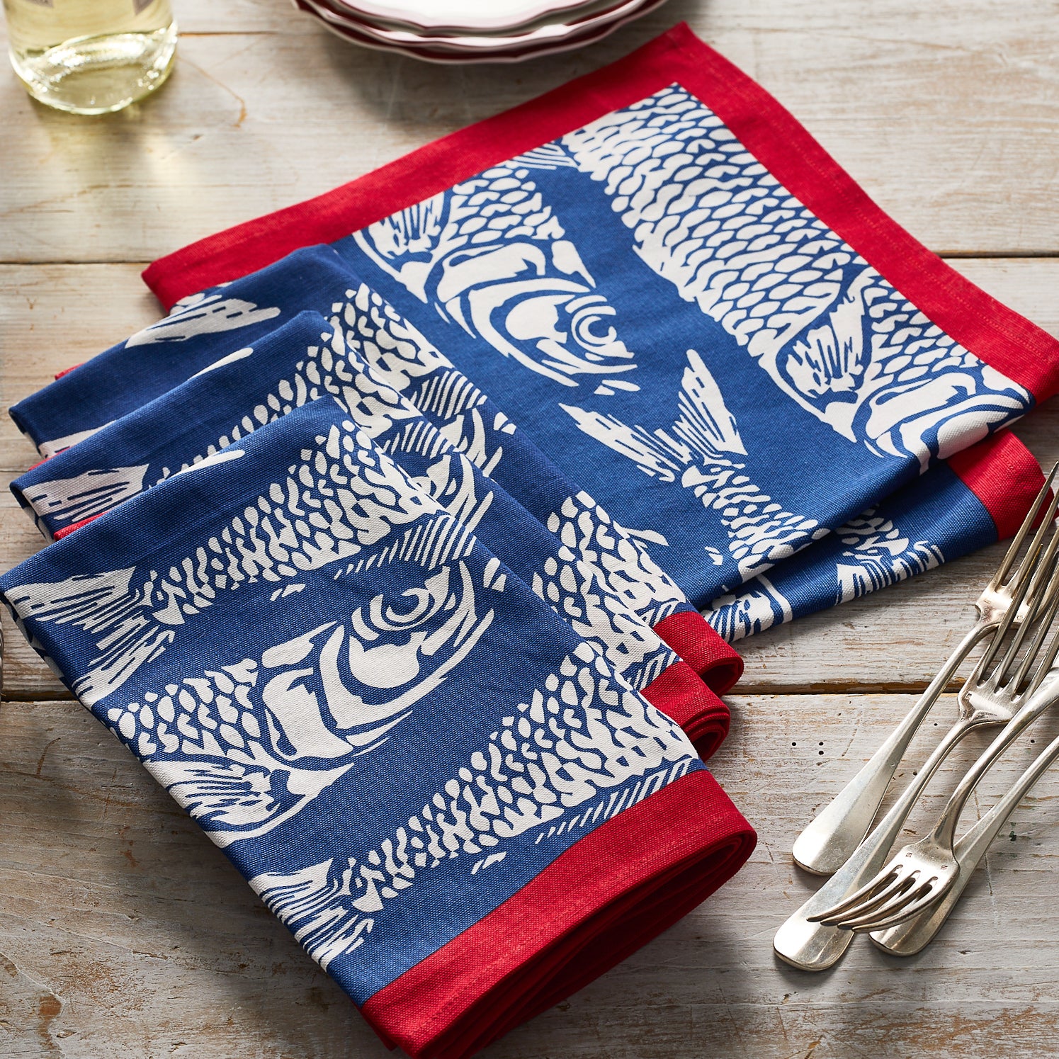 The Sardines Dinner Napkins by Caskata, set of 4, feature a playful blue and white sardine design with red borders—perfect for adding charm to your table setting.