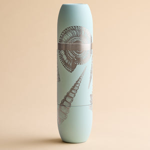 A Caskata x High Camp light blue cylindrical insulated wine flask featuring silver seashell illustrations on a beige background.