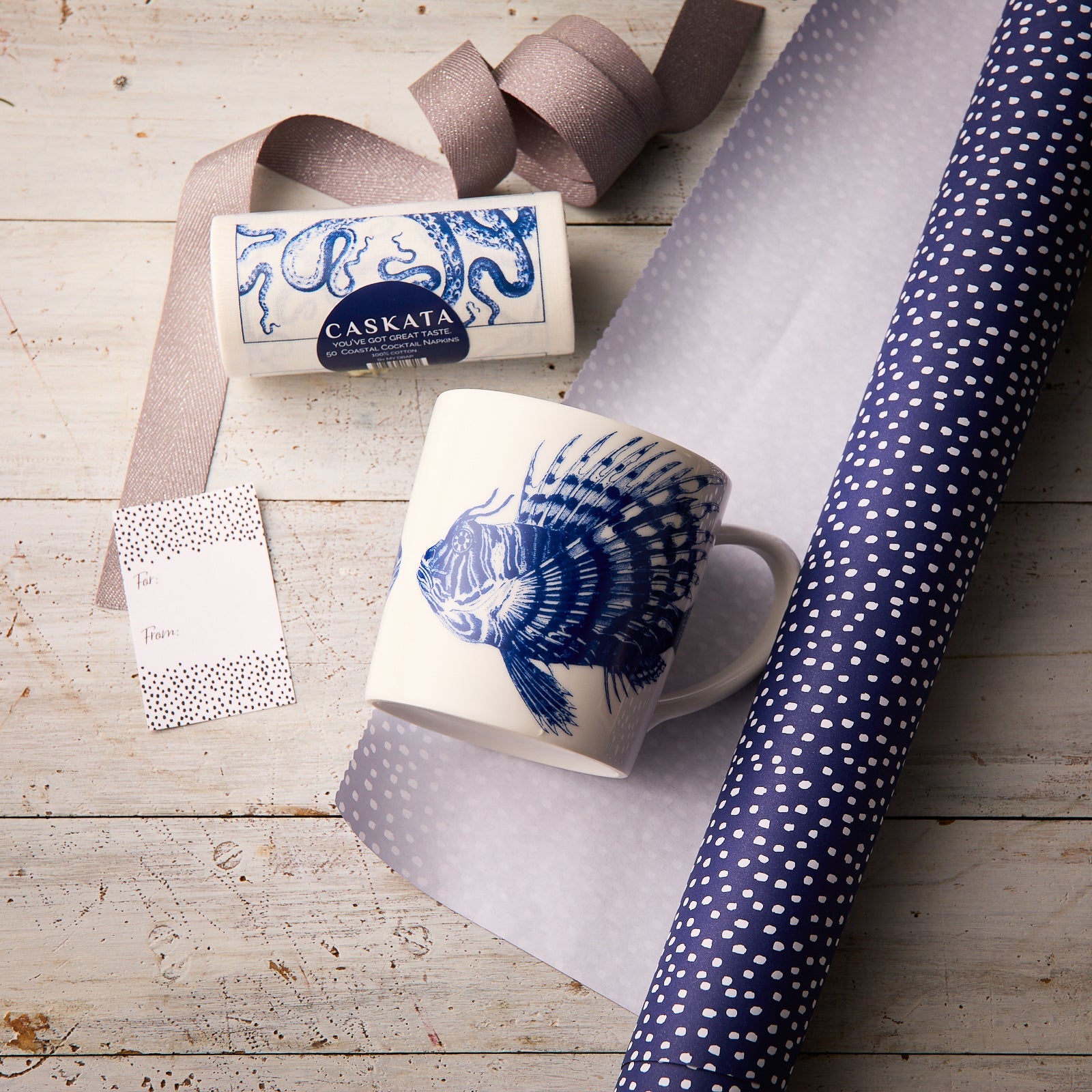 The Ella in the Morning Bundle by Caskata features a spiky fish mug with blue fish design, soap, ribbon, gift tag, and polka dot wrapping—an ideal beach lover gift.