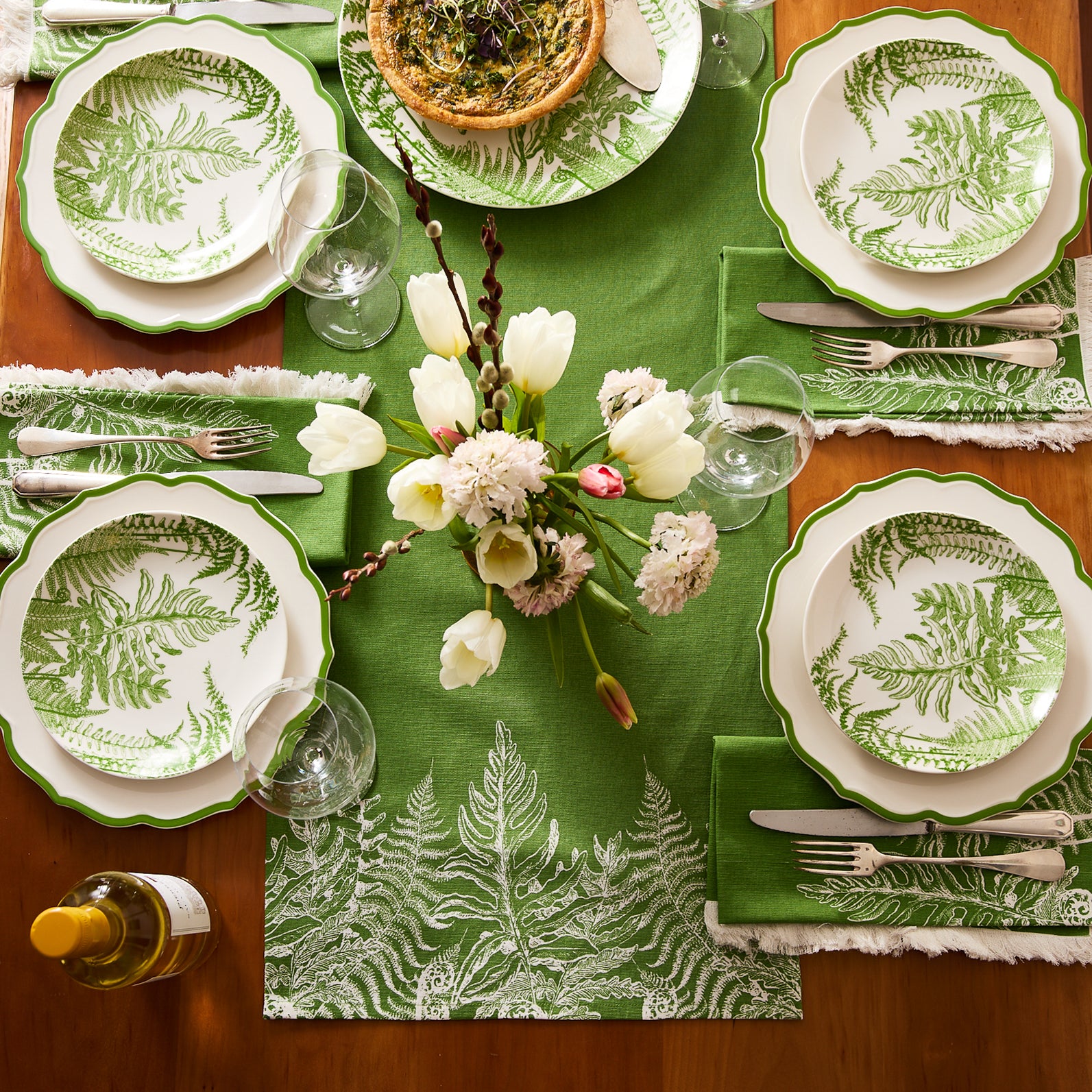 The Gardener's Deluxe Bundle by Caskata includes green fern-patterned porcelain salad plates, botanical cocktail napkins, a vase, and a round plate with orange flowers and green vines.