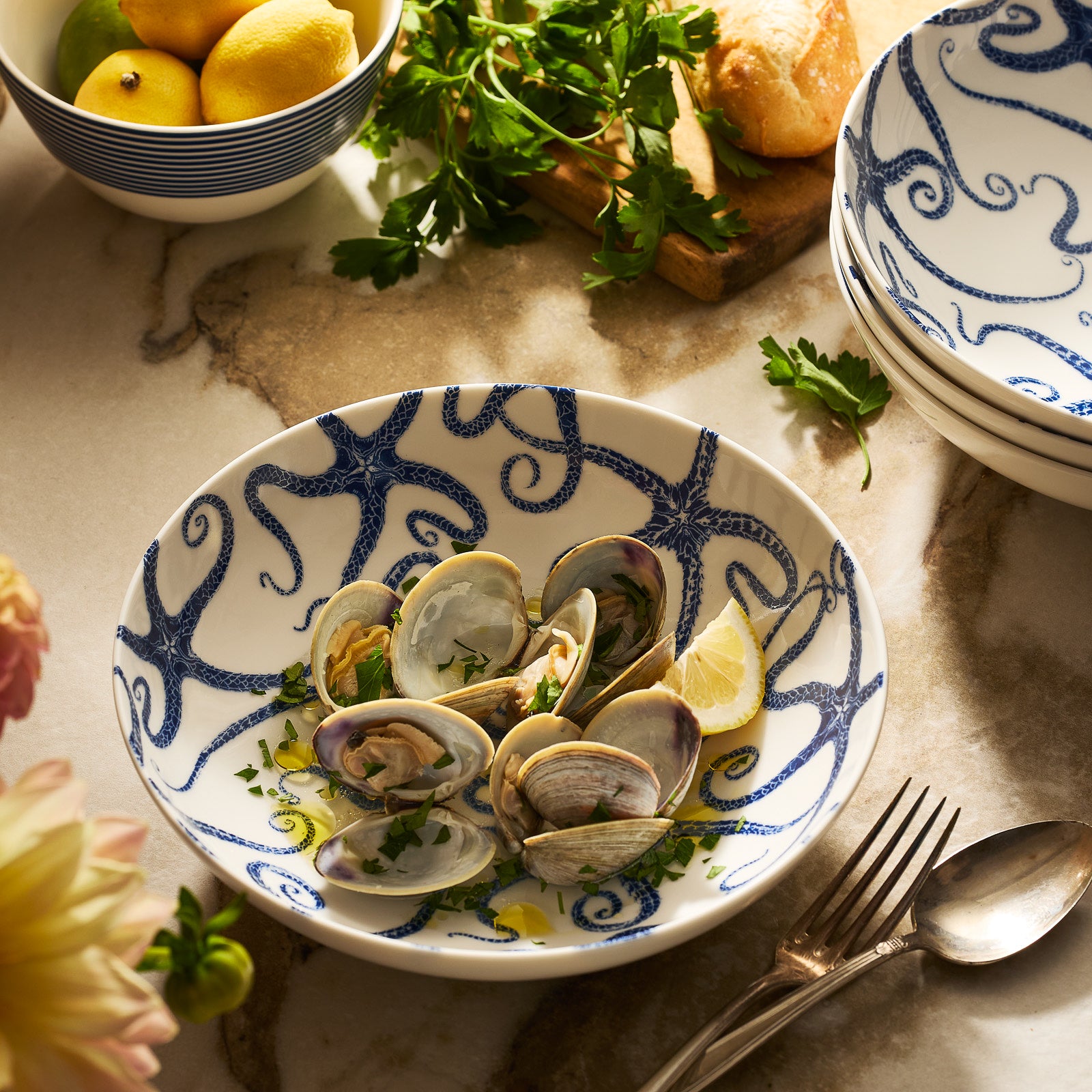 Caskata’s Starfish Entrée Bowl, viewed from above against a light beige background, features a white ceramic design adorned with a blue starfish motif, capturing the essence of coastal charm.