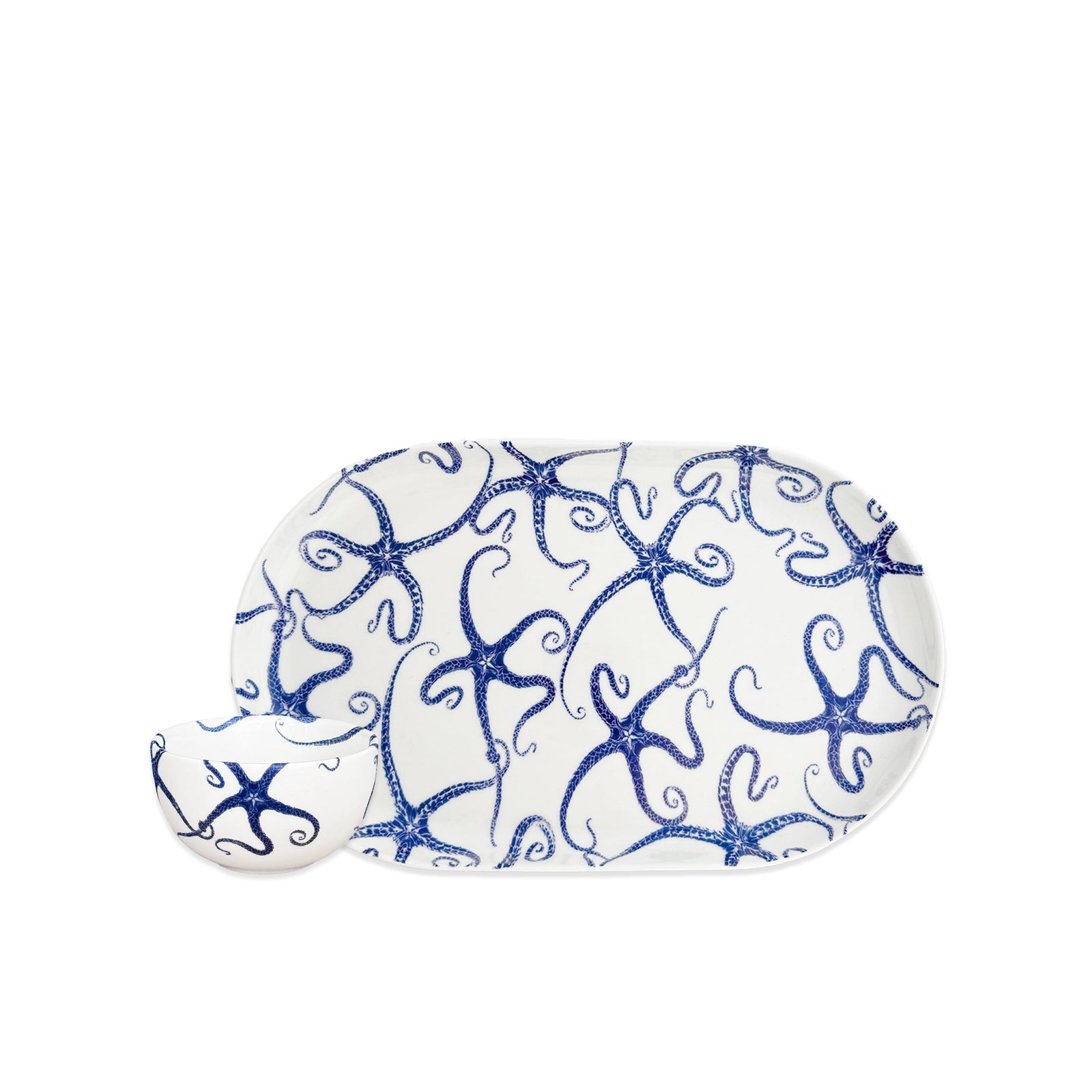 The Caskata Starfish Crudité Set includes an oval porcelain platter and small bowl with a blue starfish pattern on white—perfect as a serving or appetizer dish.