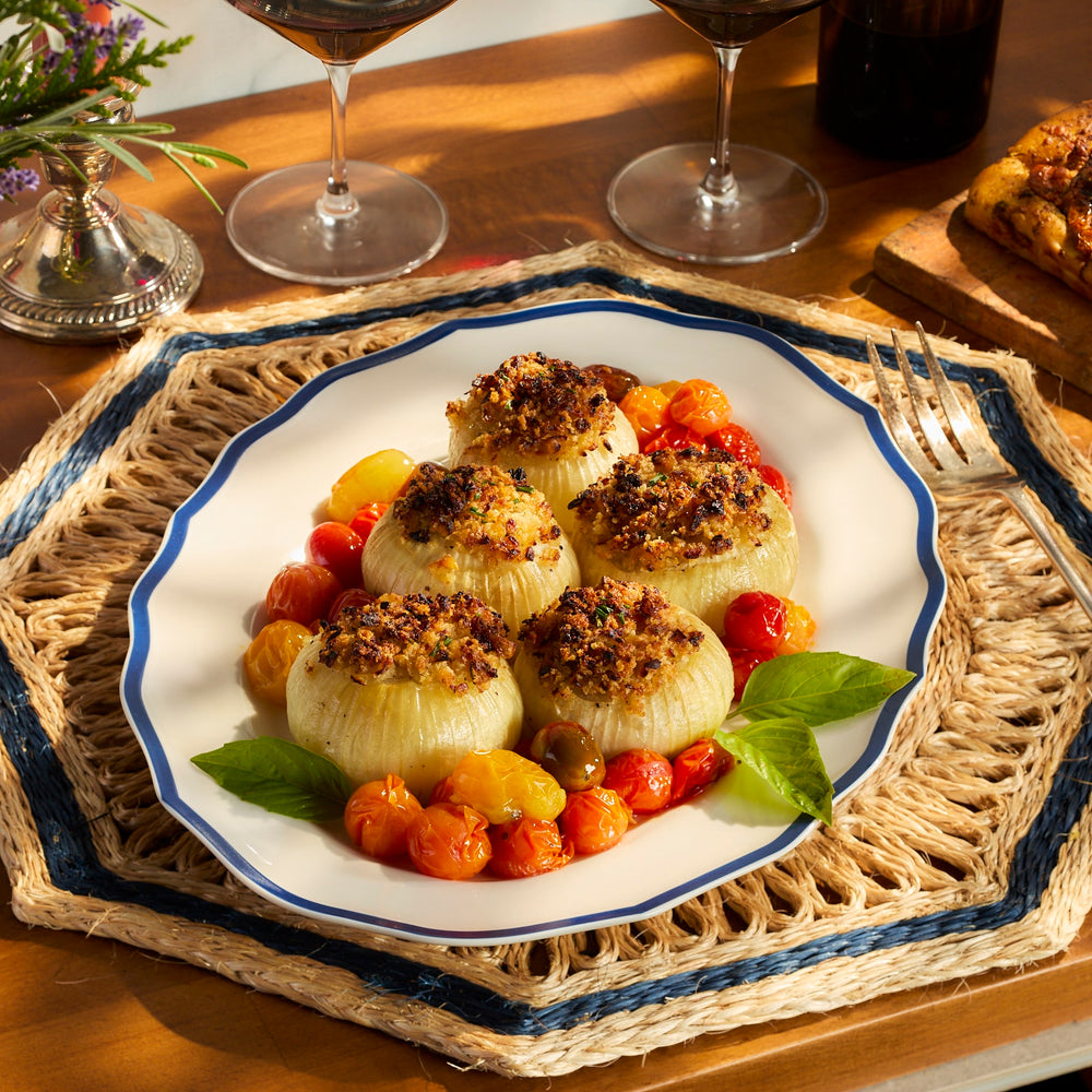 Stuffed onions topped with breadcrumbs and surrounded by roasted cherry tomatoes on a Caskata Stella Blue Scalloped Platter.