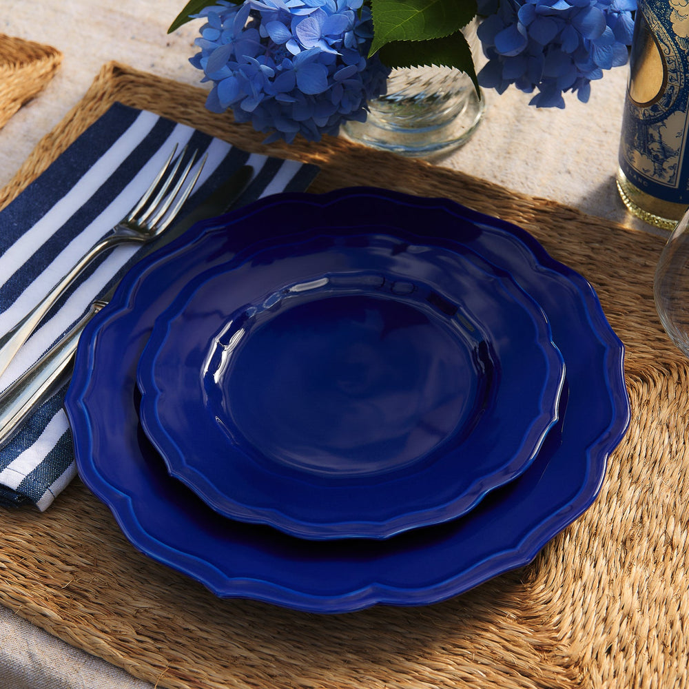 Two Stella Scalloped Solid Blue Salad Plates stacked on a woven placemat with a striped napkin and silverware.