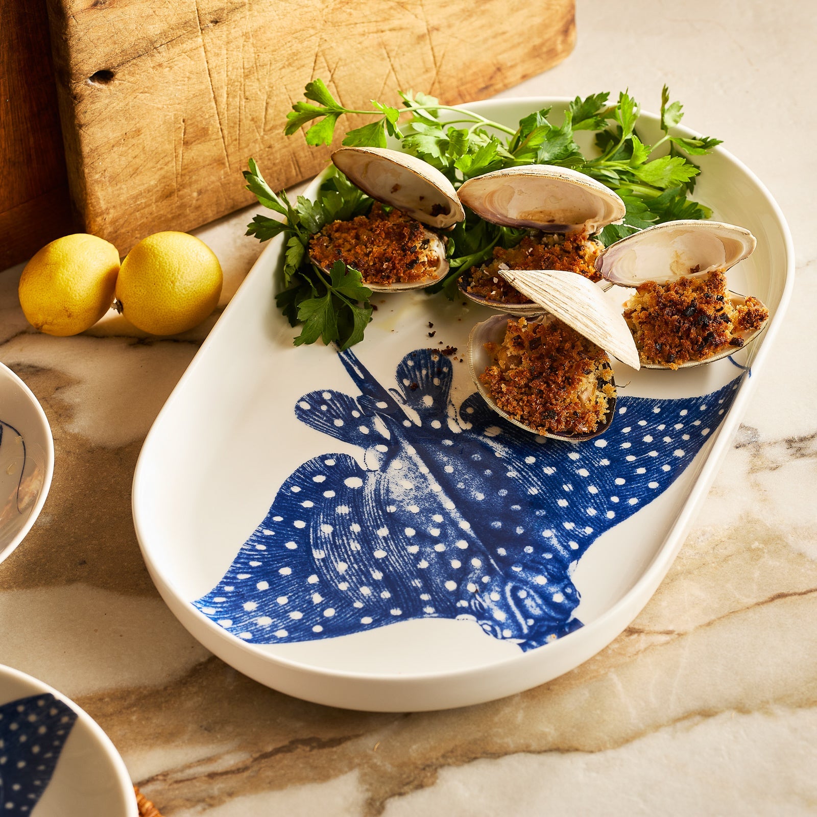 The Caskata Ray the Stingray Large Coupe Oval Platter showcases a blue spotted stingray with a long tail, bringing coastal charm and elegance to your gatherings.