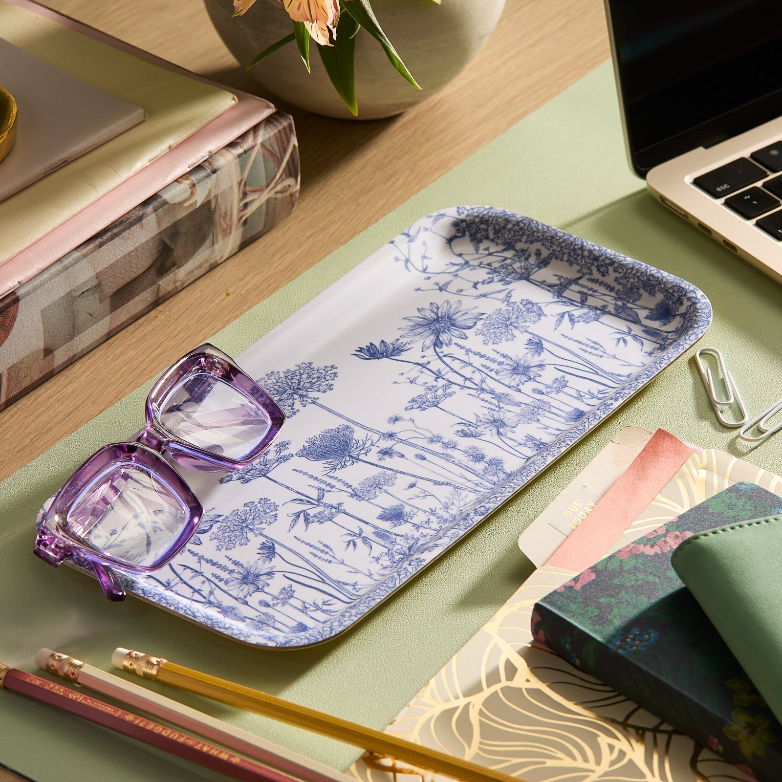 The Caskata Blooming Blues Bundle, featuring a wildflower serving tray and matching blue botanical cotton kitchen towels, is styled with ribbon, scissors, and gift wrap on a rustic white table for a charming cottagecore look.
